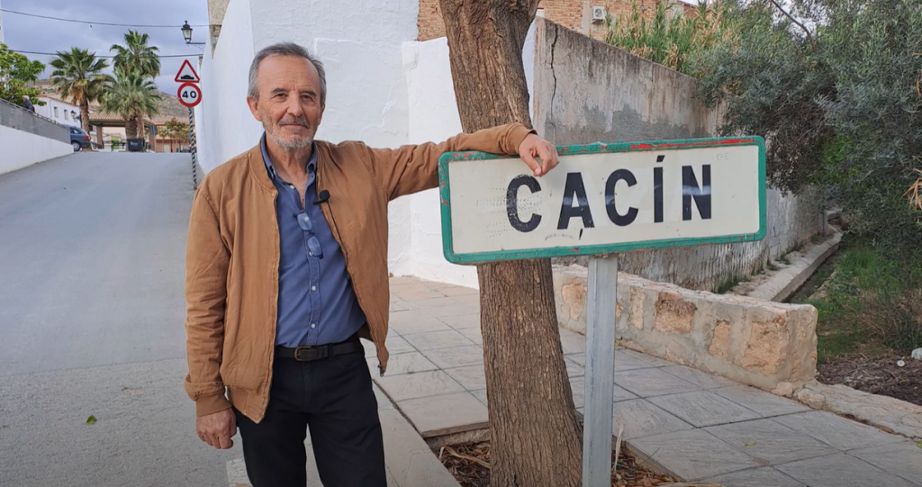 Miguel Ángel Pérez Abad junto al cartel de Cacín, su pueblo natal y fuente de inspiración para su obra "El río y otros relatos: Cacín revisitado"